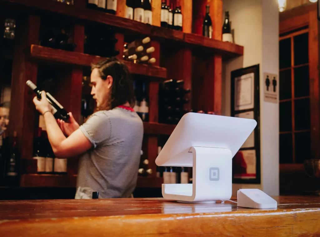 waitress behind the bar inside a restaurant, holding a bottle of wine.
